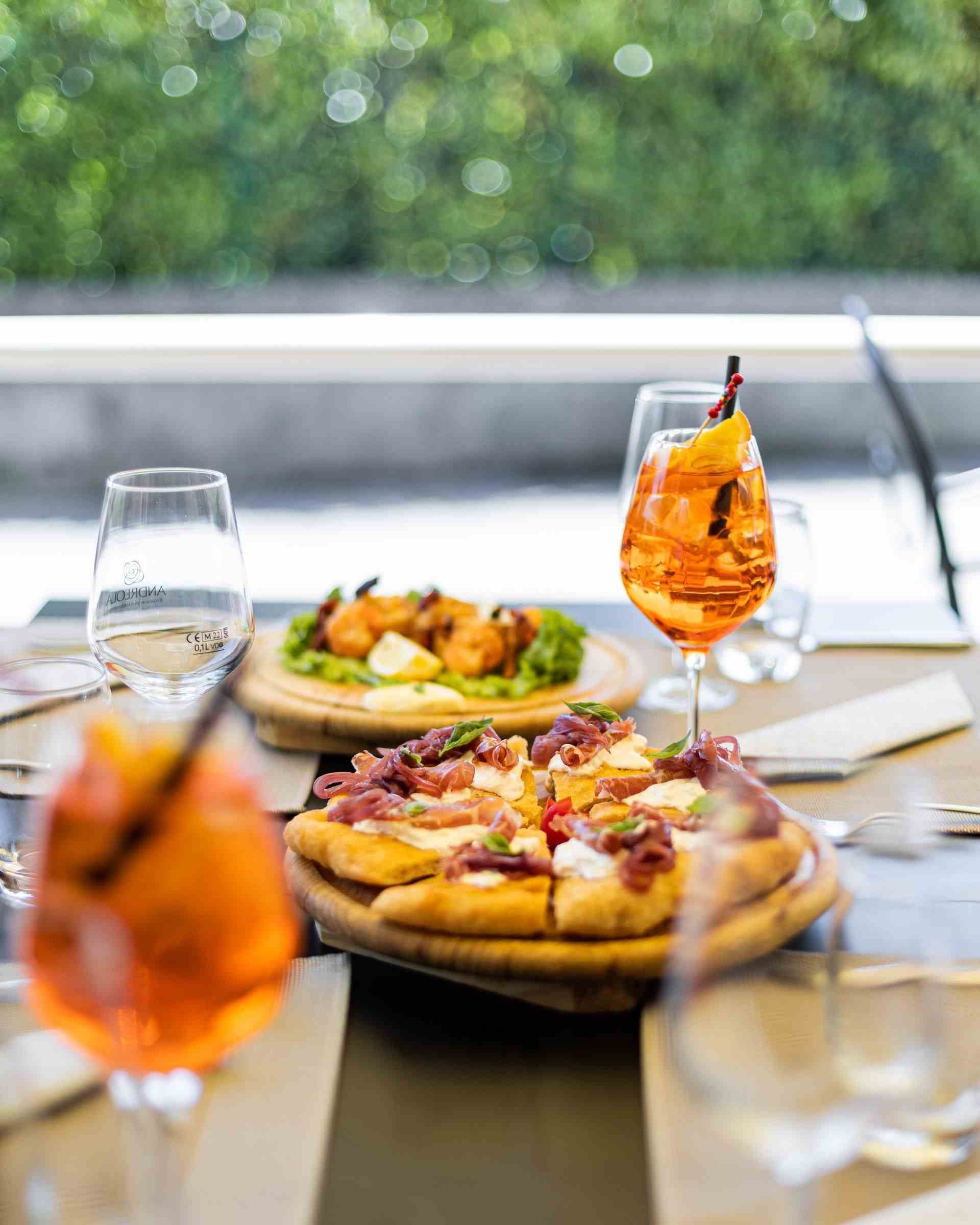 Table dressée avec pizzas, amuse-gueules et cocktails ; cadre extérieur.
