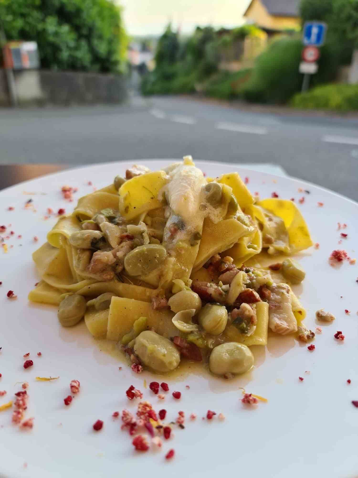Plat de pâtes aux fèves et au bacon sur une assiette blanche, scène de rue en arrière-plan.