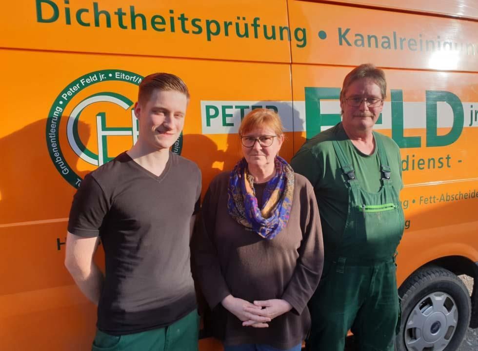 Drei Personen stehen vor einem orangefarbenen Lieferwagen 