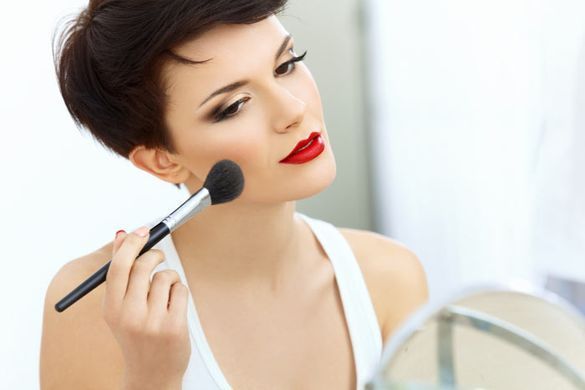 Una mujer se aplica maquillaje en la cara frente a un espejo.
