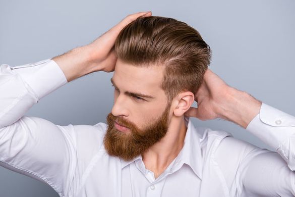 Un hombre con barba y camisa blanca se toca el pelo.