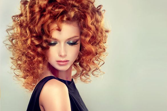 Una mujer con cabello rojo y rizado lleva un vestido negro.