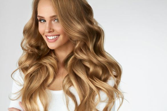 Una mujer con cabello largo y ondulado sonríe y viste una camisa blanca.