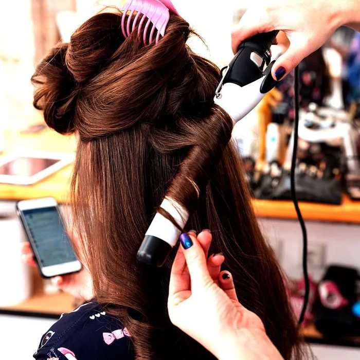 Una mujer se está rizando el cabello con un rizador.