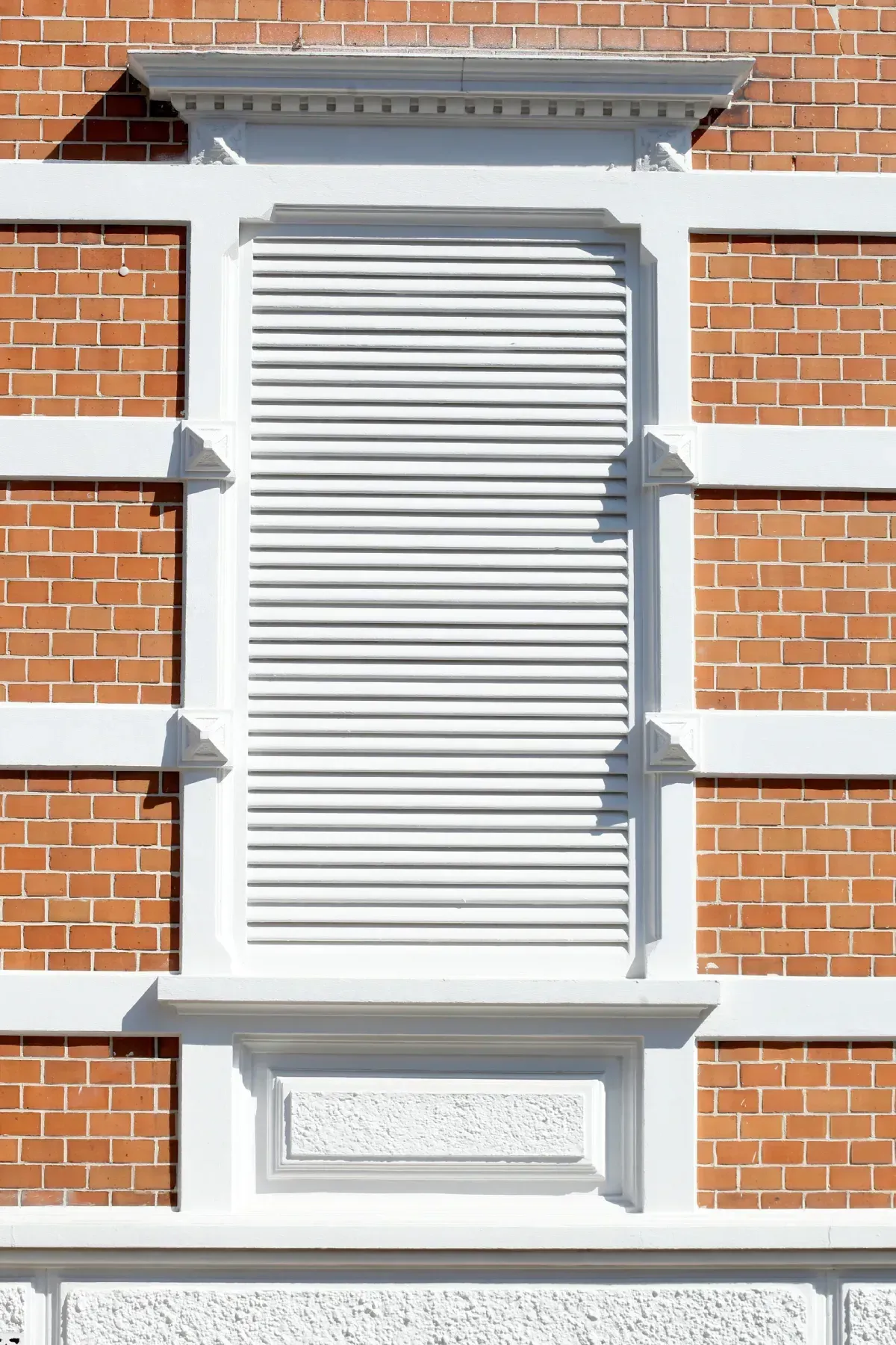 Ventana con contraventanas blancas en fachada de ladrillo con molduras blancas.