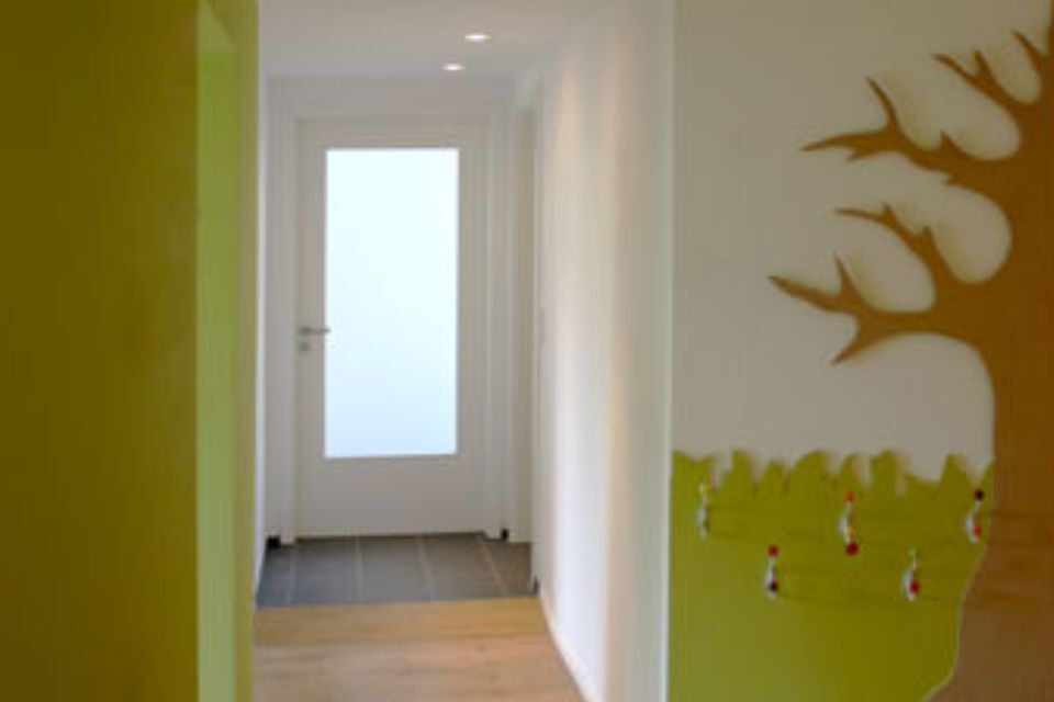 Flur mit weißer Tür am Ende, grünen Wänden, Baumwandbild und Holzboden.