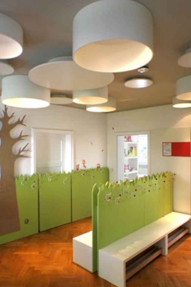 Hellgrünes und weißes Wartezimmer für Kinder mit einer Bank, Trennwänden und runden Hängelampen.