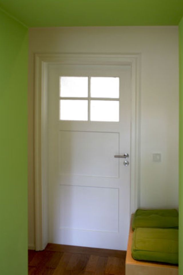 Weiße Innentür mit Glasscheiben und silbernem Griff in einem Flur mit grünen Wänden.