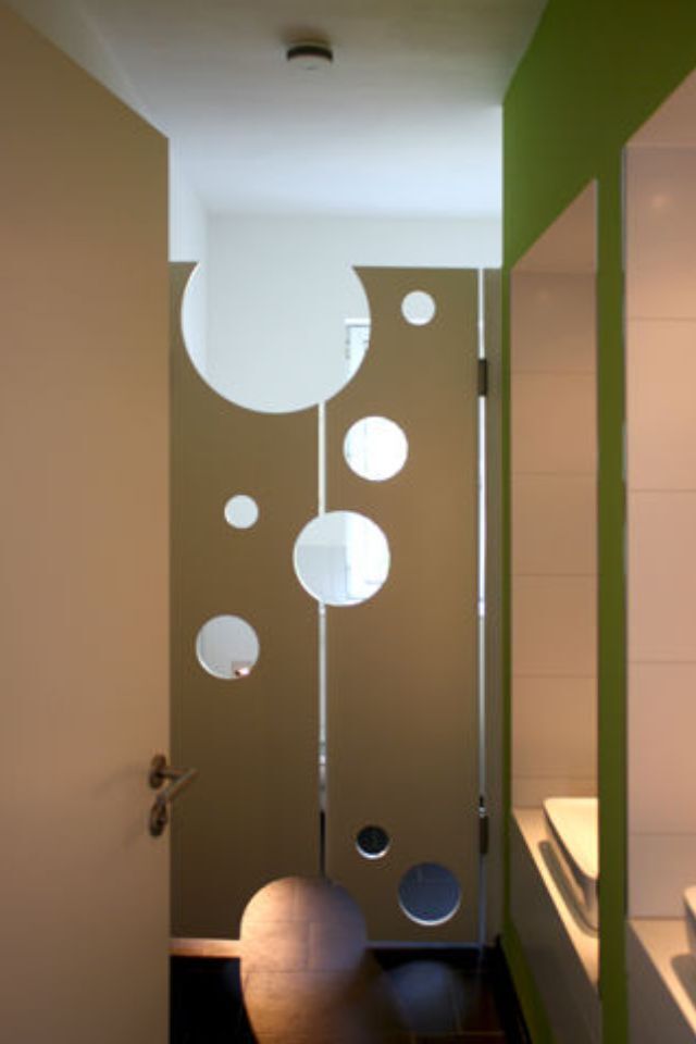 Badezimmer mit hellbrauner Tür, kreisförmigen Ausschnitten und grüner Wand.