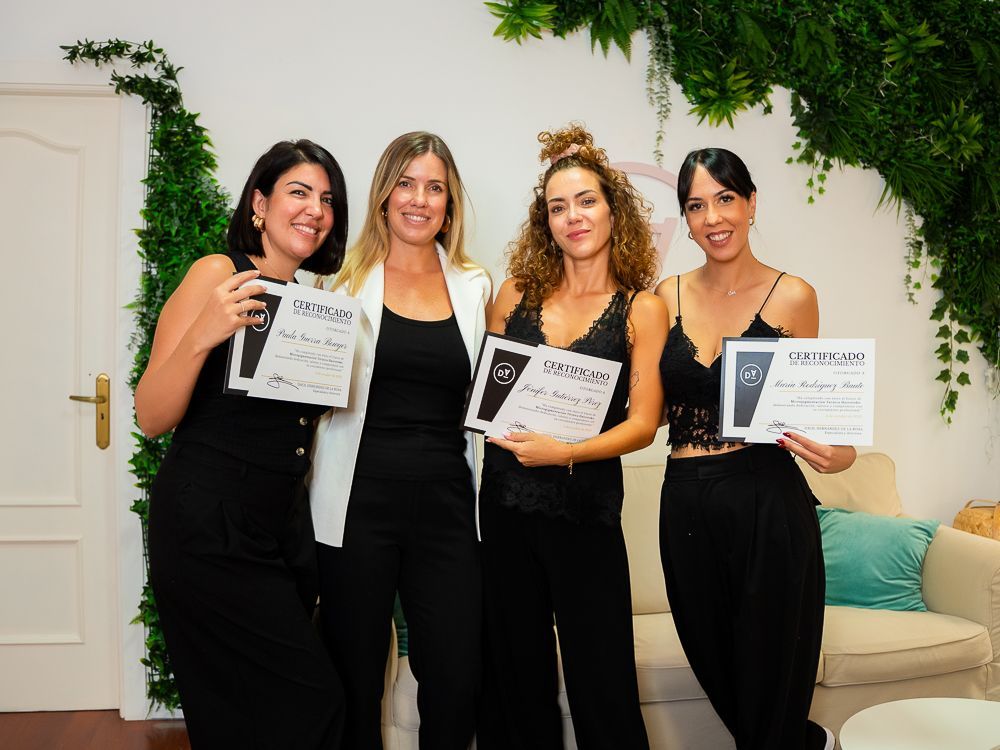 Cuatro mujeres vestidas de negro sosteniendo certificados, sonriendo frente a un follaje verde.