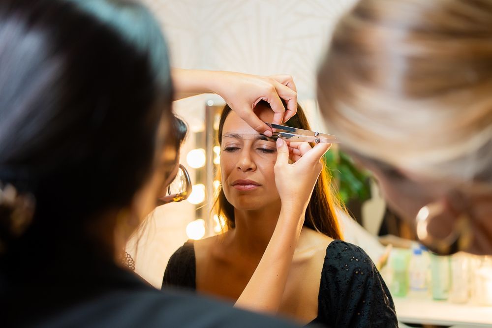 El maquillador recorta la ceja del cliente con unas tijeras pequeñas en un estudio luminoso.