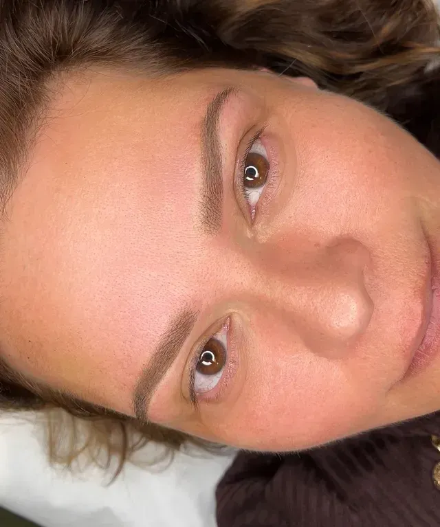 Primer plano de una persona con las cejas recién tatuadas. Tiene cejas de color marrón claro y ojos marrones.