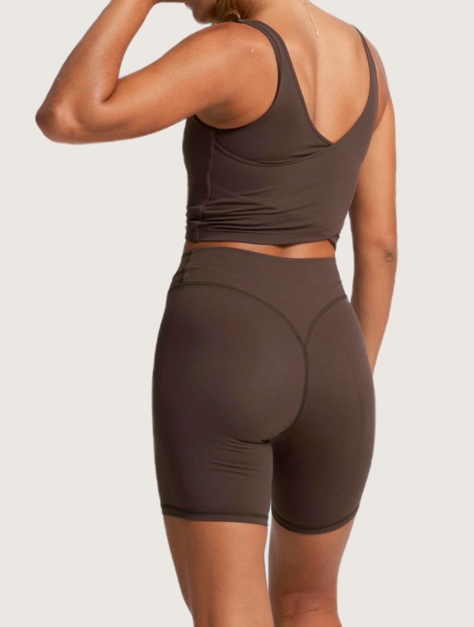 Eine Person in brauner Sportkleidung zeigt die Rückseite eines eng anliegenden Tanktops und Shorts.
