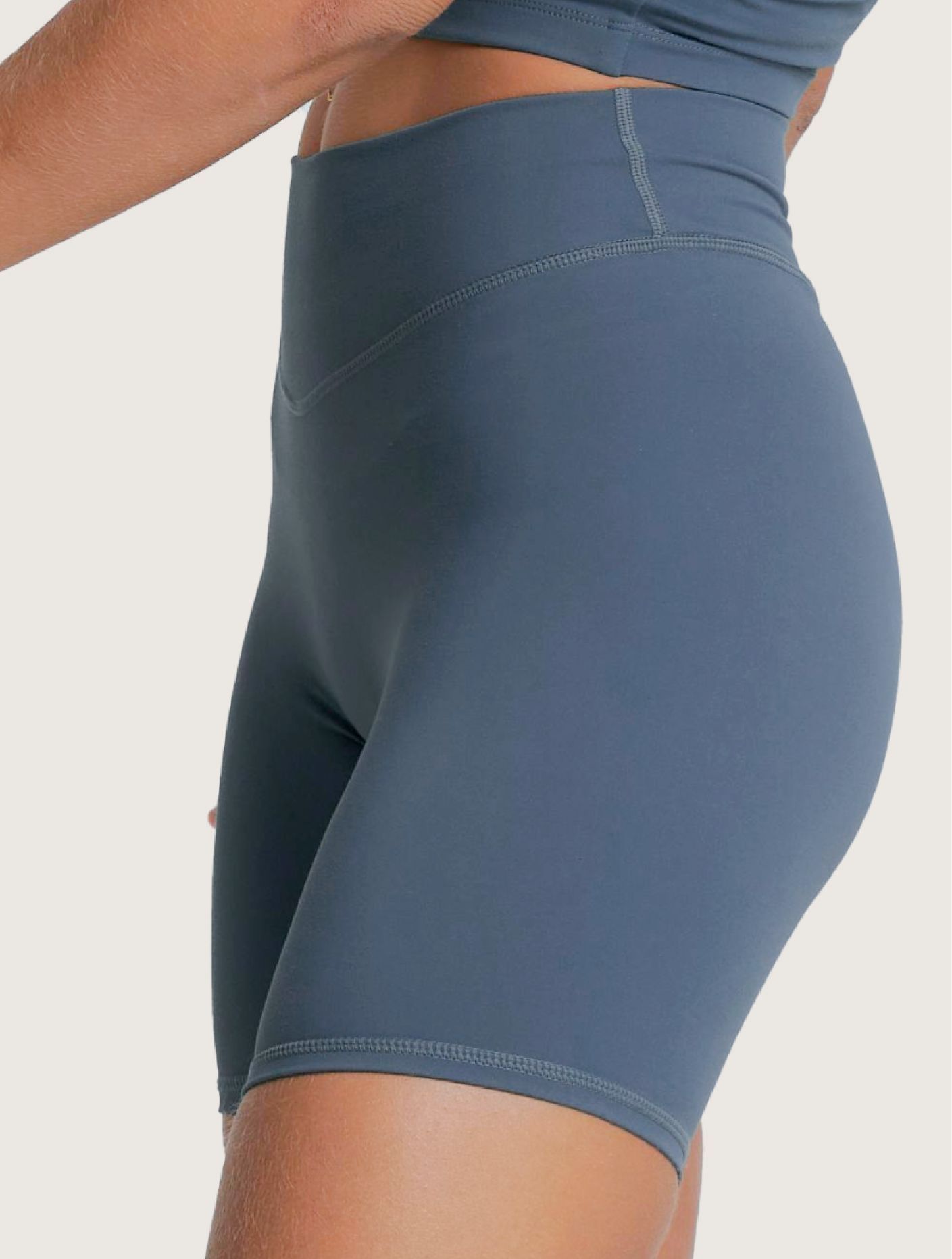 Frau in blauem Sportoutfit mit eng anliegendem Crop-Top und Shorts, die mit den Händen in den Hüften steht.