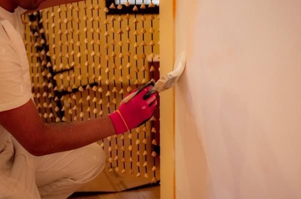 Un hombre se arrodilla y pinta una pared con un pincel.