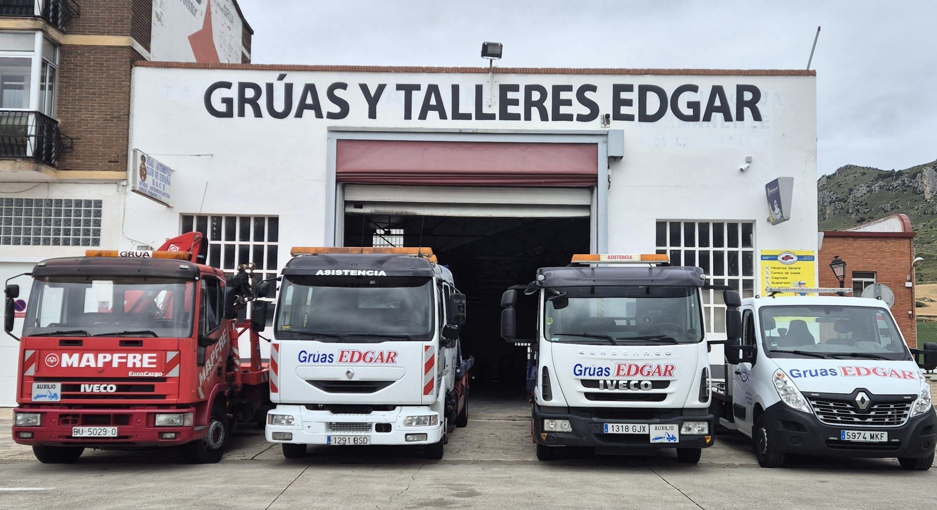 Un grupo de camiones están estacionados frente a un edificio que dice gruas y talleres edgar