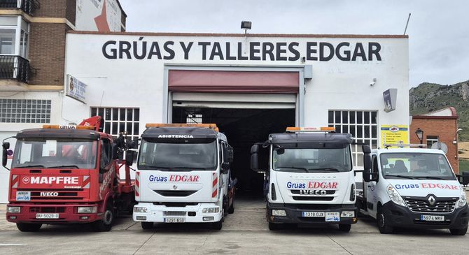Un grupo de camiones están estacionados frente a un edificio que dice gruas y talleres edgar