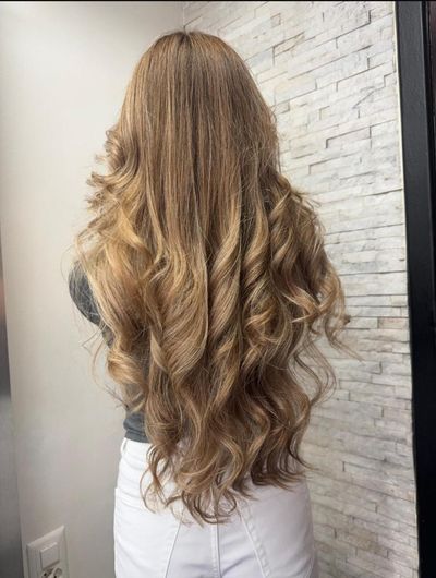 Frau mit blondem, gewelltem und halb hochgestecktem Haar, das mit Haaraccessoires verziert ist, sitzt in einem Friseurstuhl.