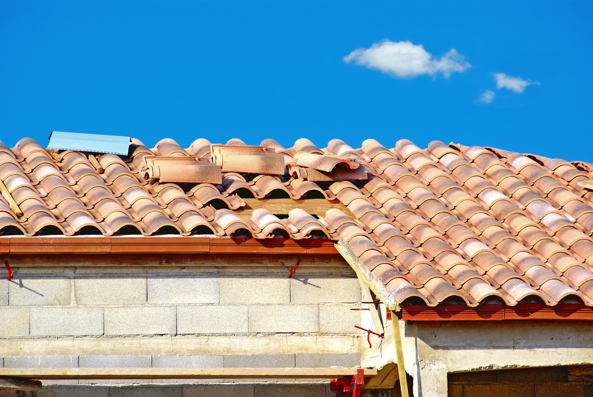 Toiture en construction avec tuiles manquantes et ciel bleu.