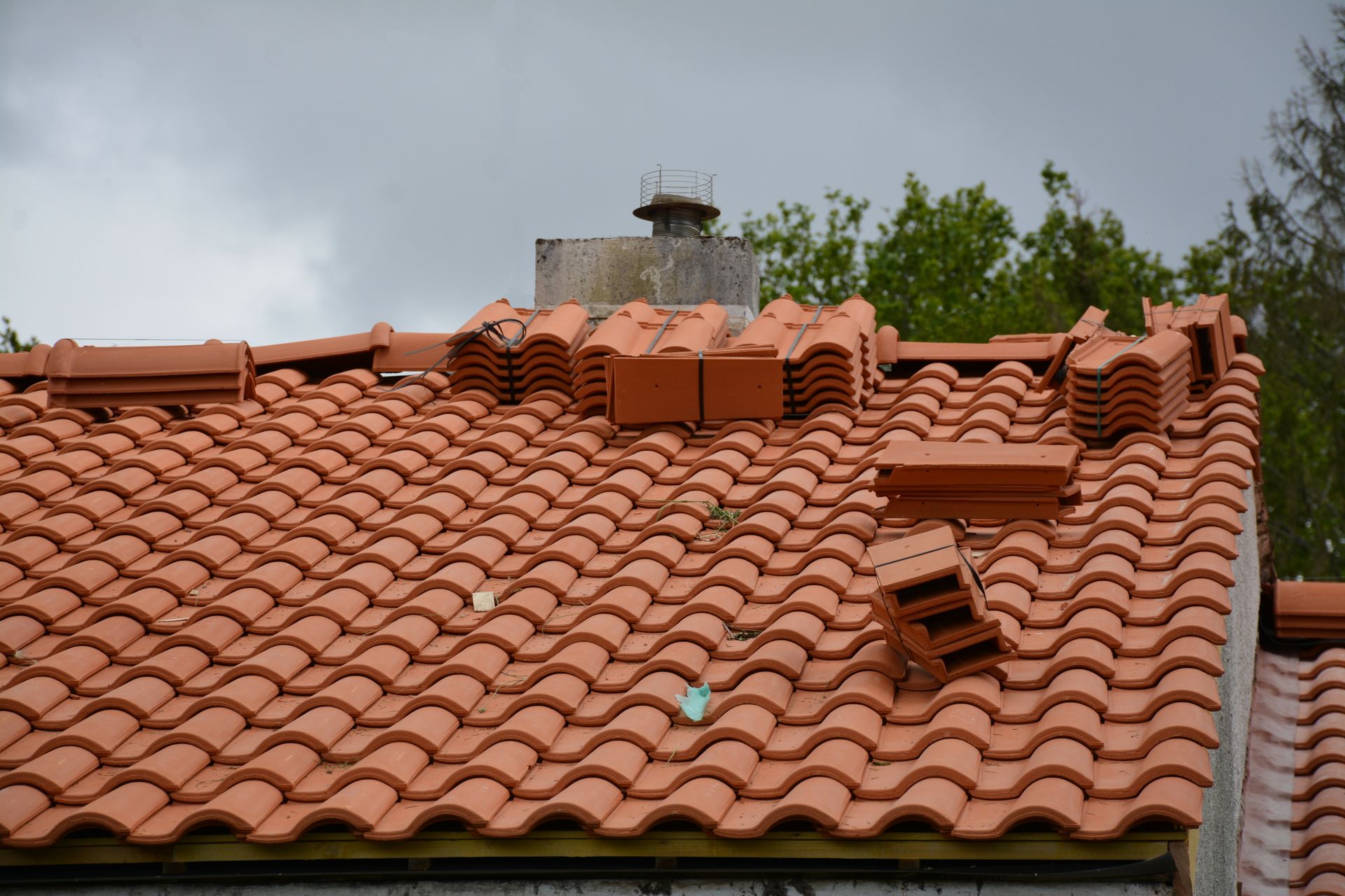 Toiture en tuiles rouges avec cheminée, quelques tuiles détachées, ciel nuageux.