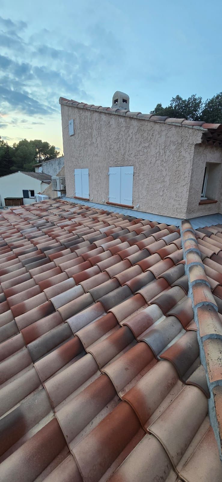 Un toit de tuiles en gros plan, avec un bâtiment texturé en arrière-plan.