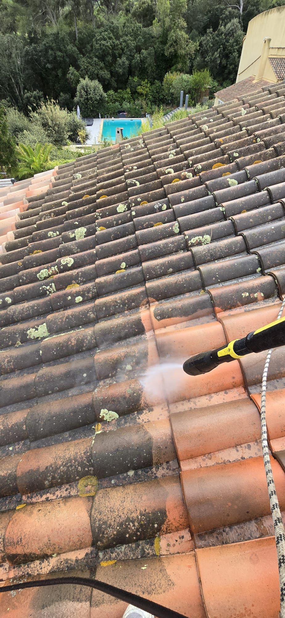 Nettoyage à haute pression d'un toit en tuiles. Nettoyeur haute pression noir et jaune pulvérisant de l'eau.