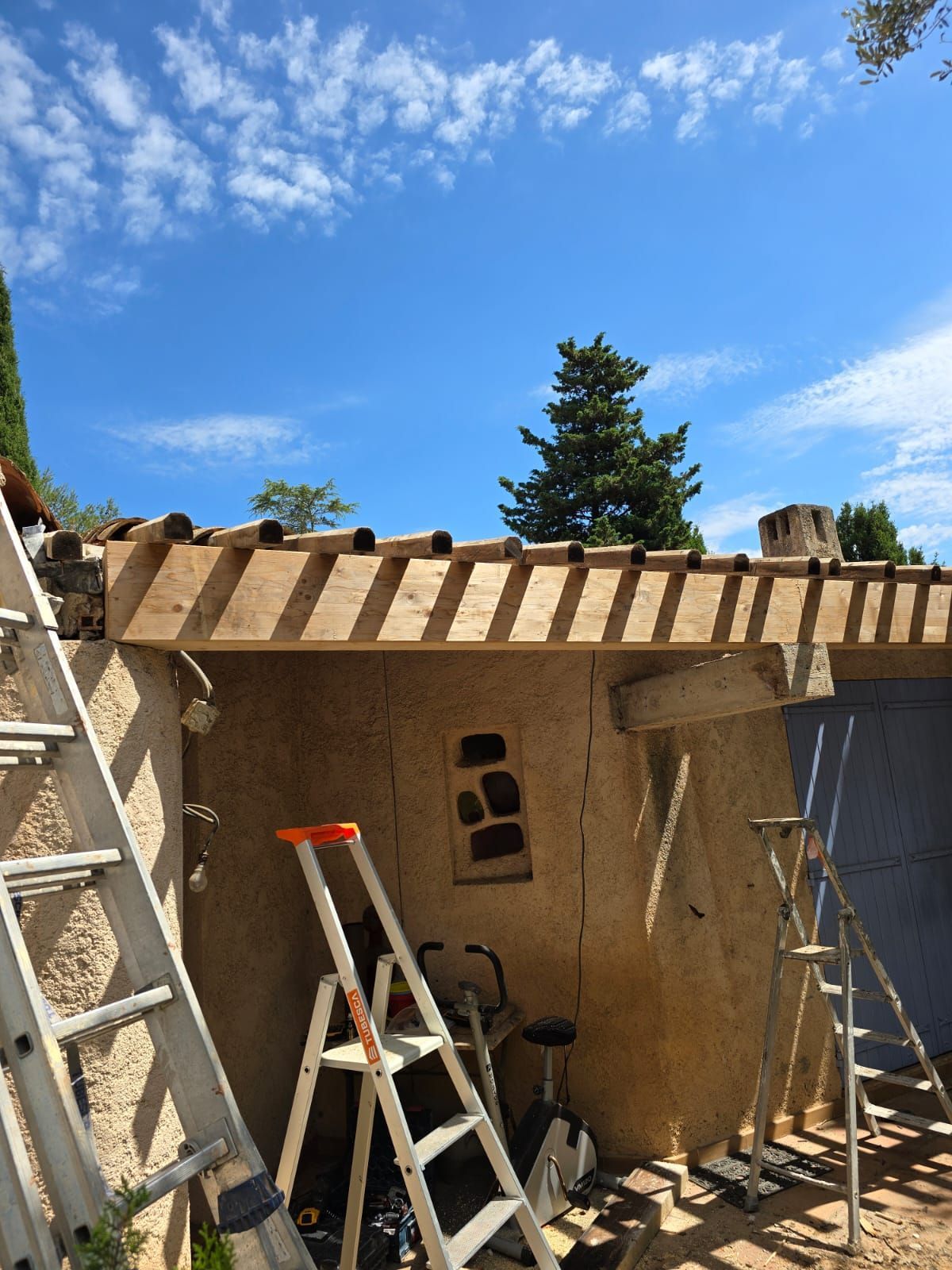 Extérieur d'un bâtiment en construction avec des échelles, un ciel bleu et un aperçu d'un arbre.