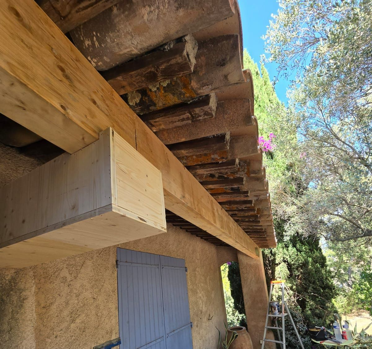 Poutres en bois soutenant un toit en tuiles, avec un caisson en contreplaqué clair fixé.