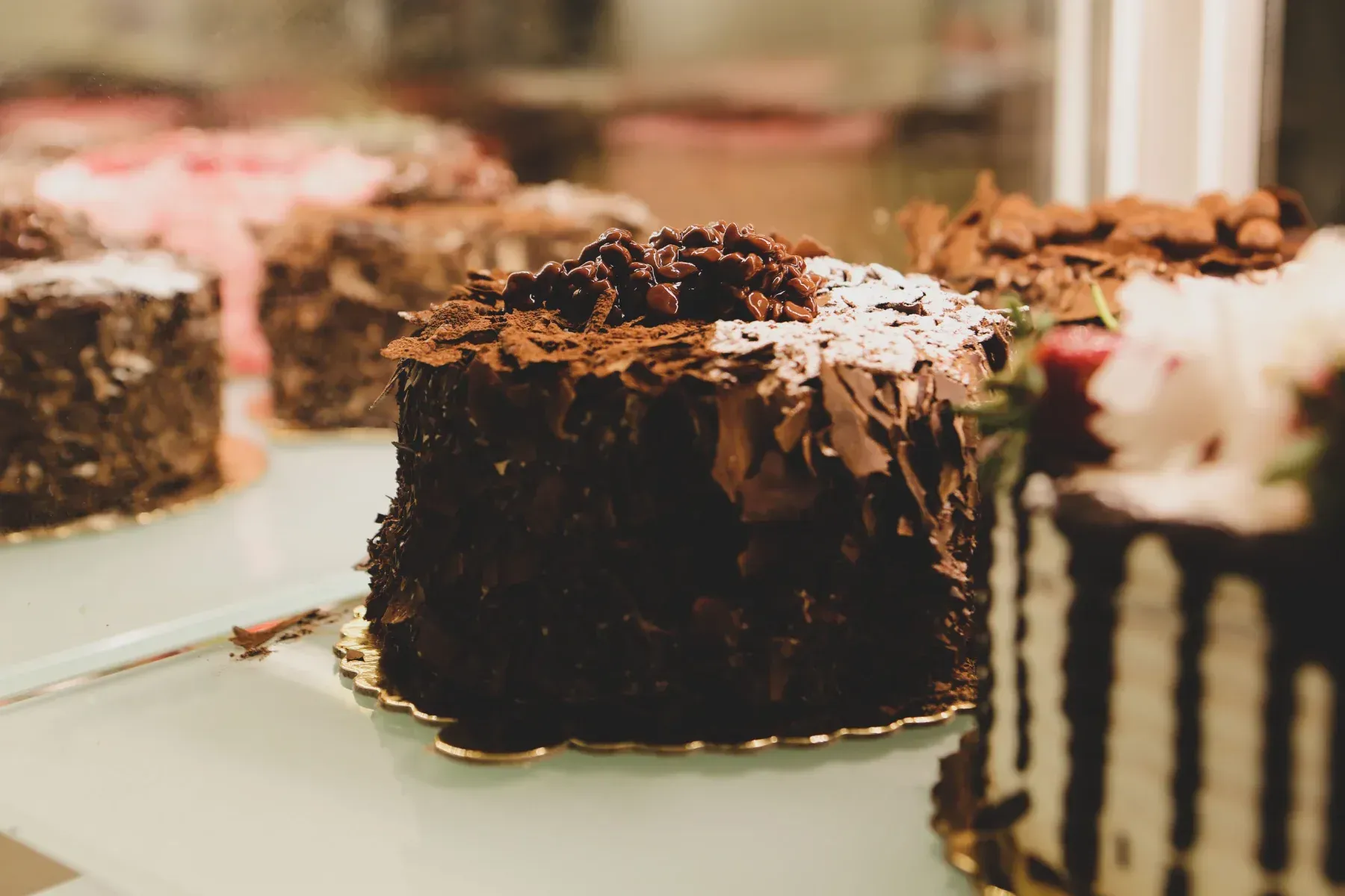 Vista de cerca de varios pasteles de chocolate exquisitos y un pastel glaseado expuestos en una vitrina de cristal 