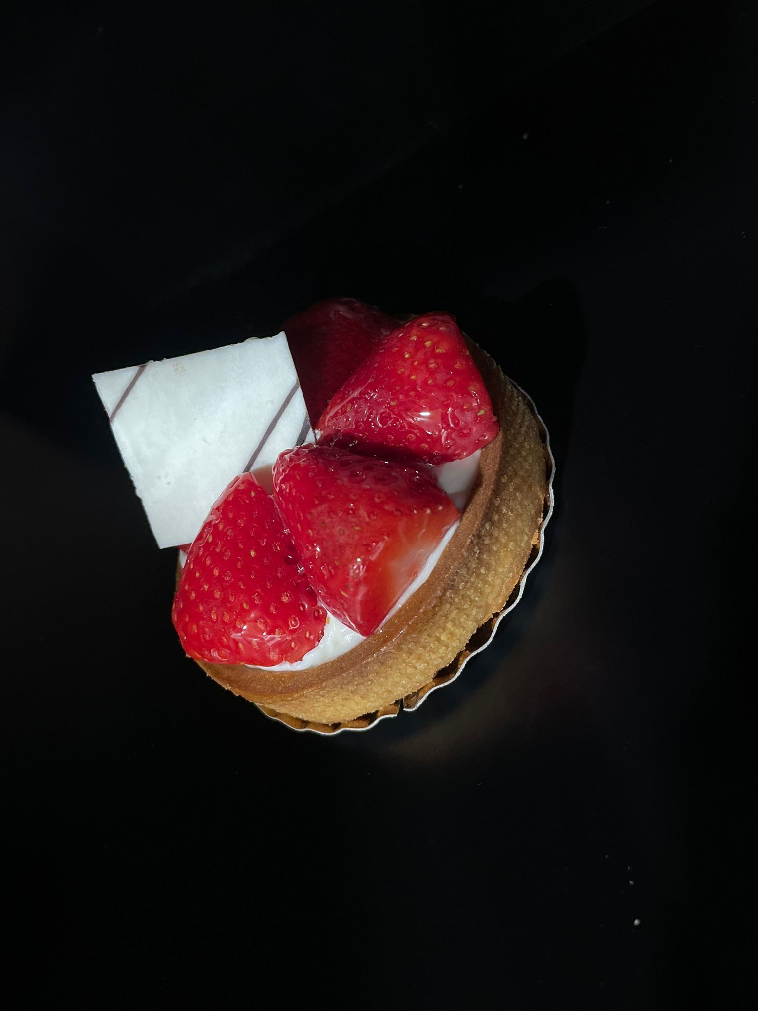 Postre con fresas en un vaso de papel sobre fondo oscuro.