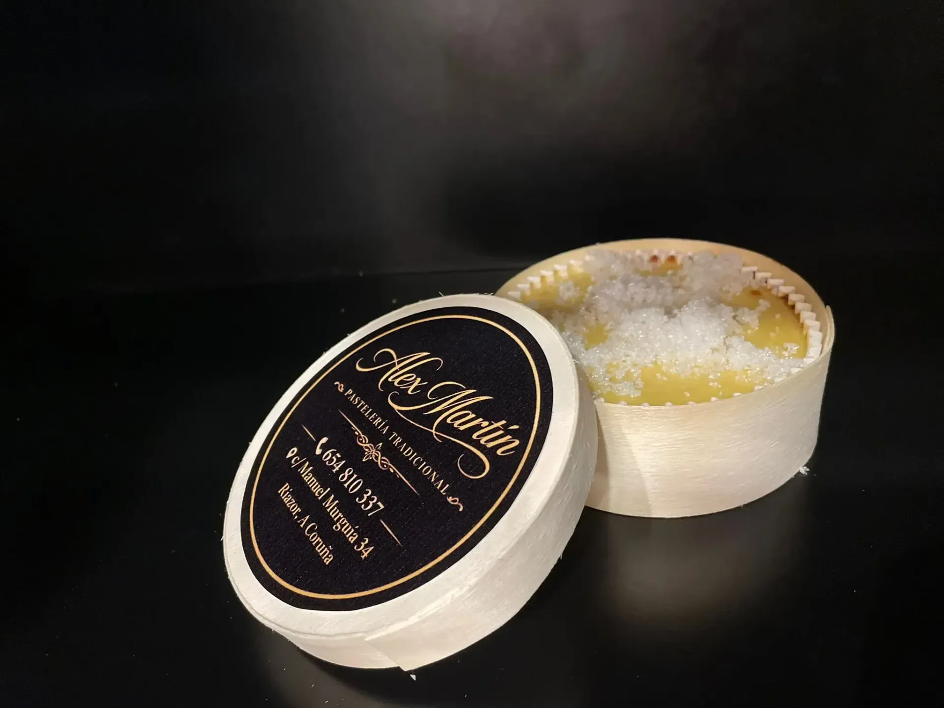 Dos pequeños tarros de cosméticos sobre una superficie oscura, uno abierto con una crema amarilla.