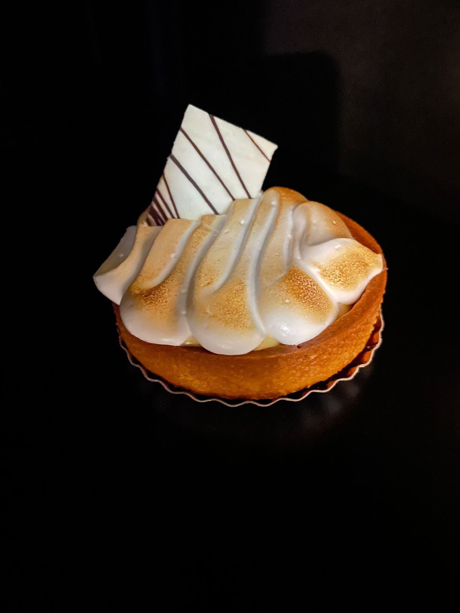 Pastel cubierto de crema con glaseado de naranja y decoración de chocolate a rayas sobre un fondo oscuro.