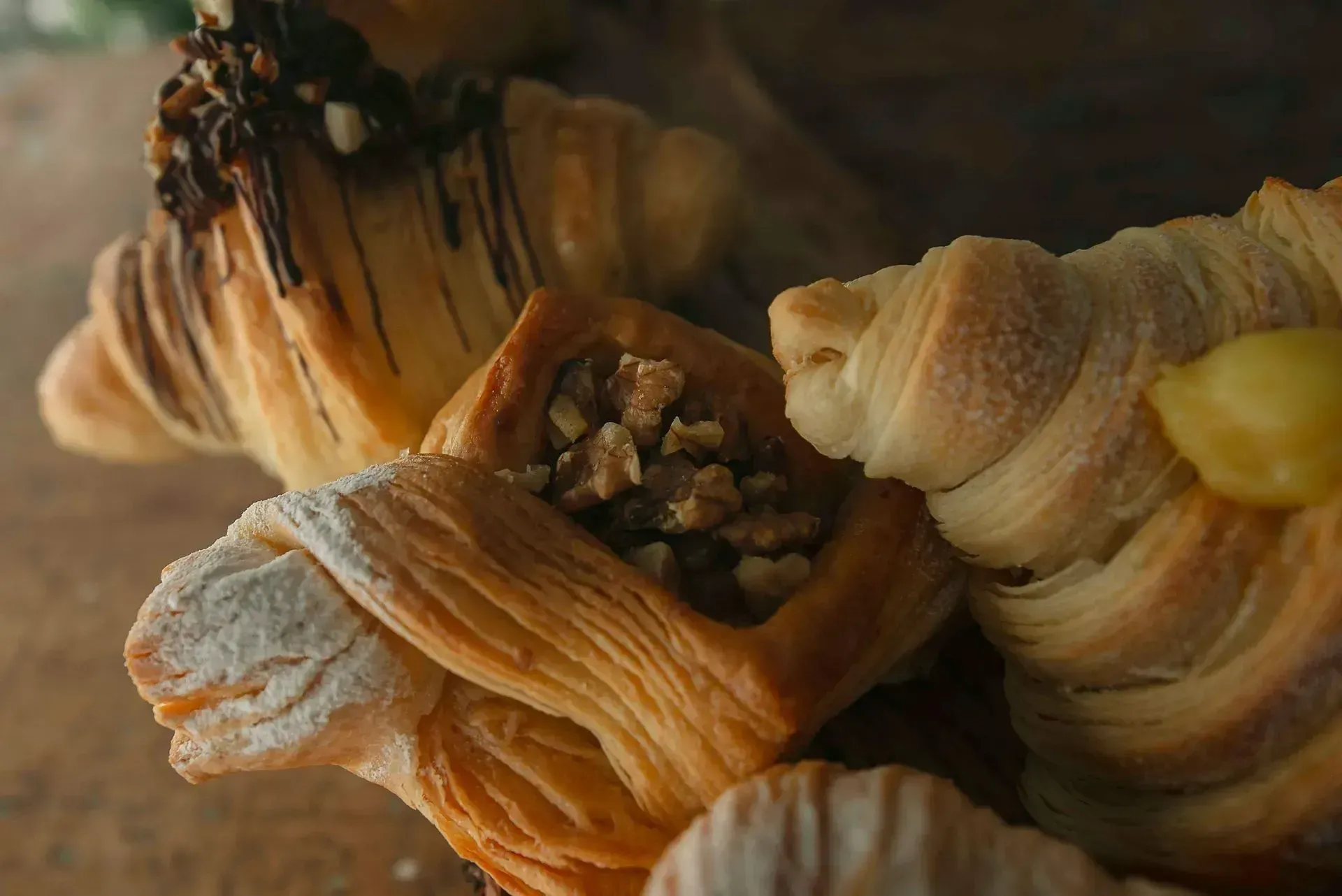 Primer plano de varios pasteles dorados y hojaldrados, cubiertos de chocolate, frutos secos