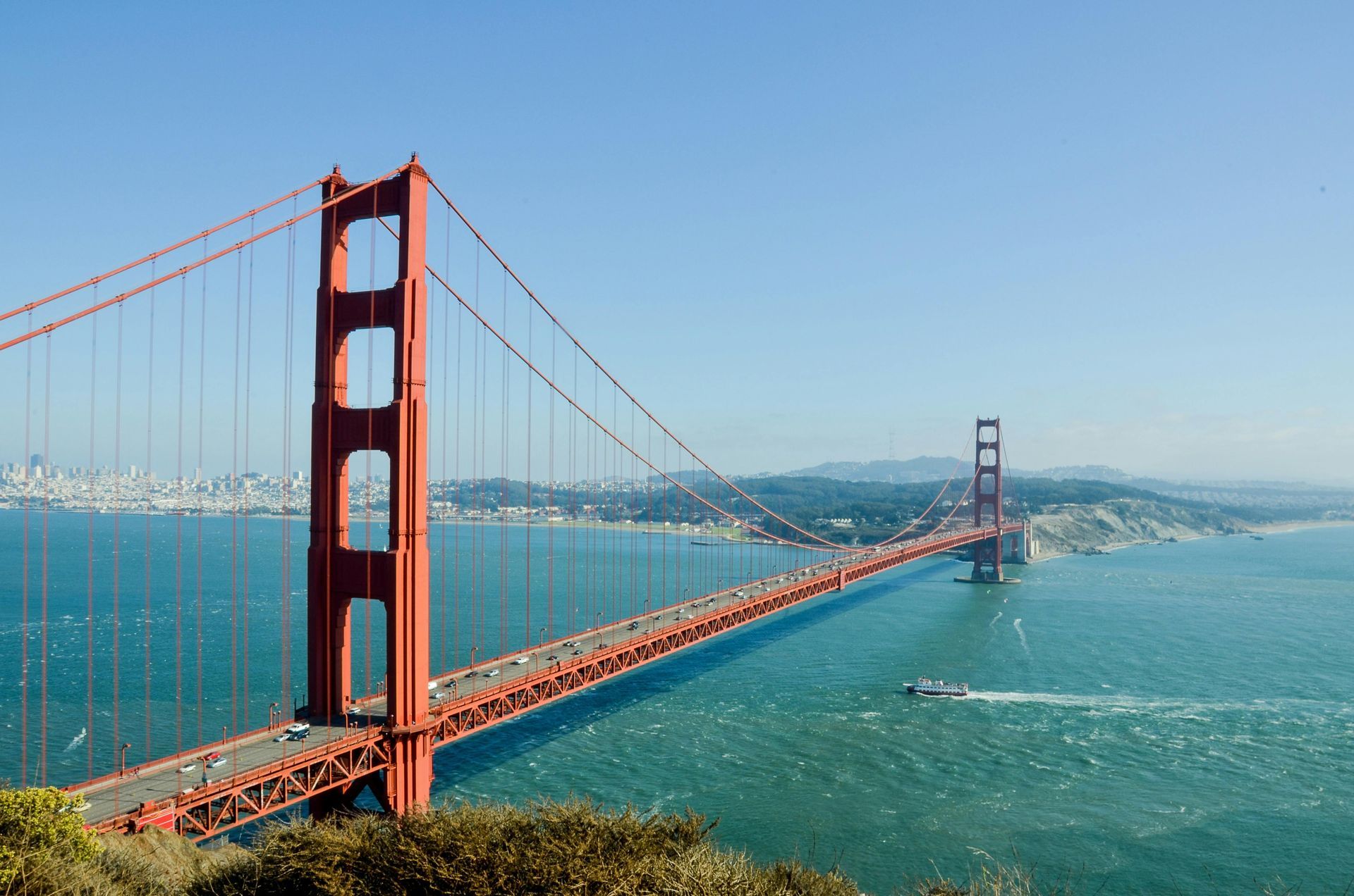 Golden Gate Bridge spans the blue water, against a city skyline and clear sky.