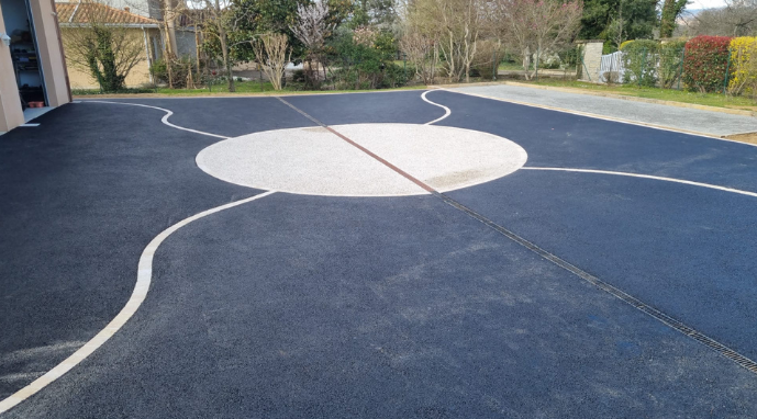 Allée en asphalte noir ornée d'un motif de cercles blancs. Des lignes blanches courbes s'étendent depuis le cercle.