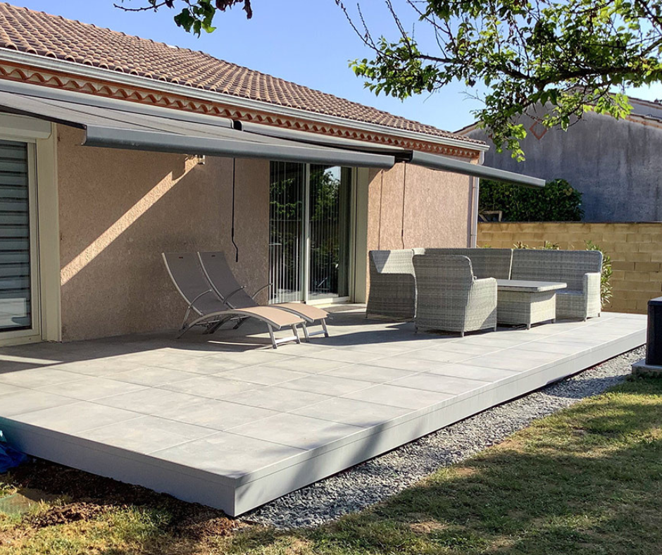 Terrasse en composite gris avec mobilier de jardin, jouxtant une maison avec un auvent.
