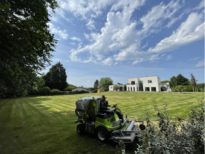 Une personne tond une pelouse verte avec une tondeuse grise et noire dans un jardin.