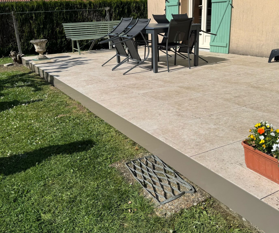 Terrasse en béton avec mobilier de jardin, donnant sur une pelouse.