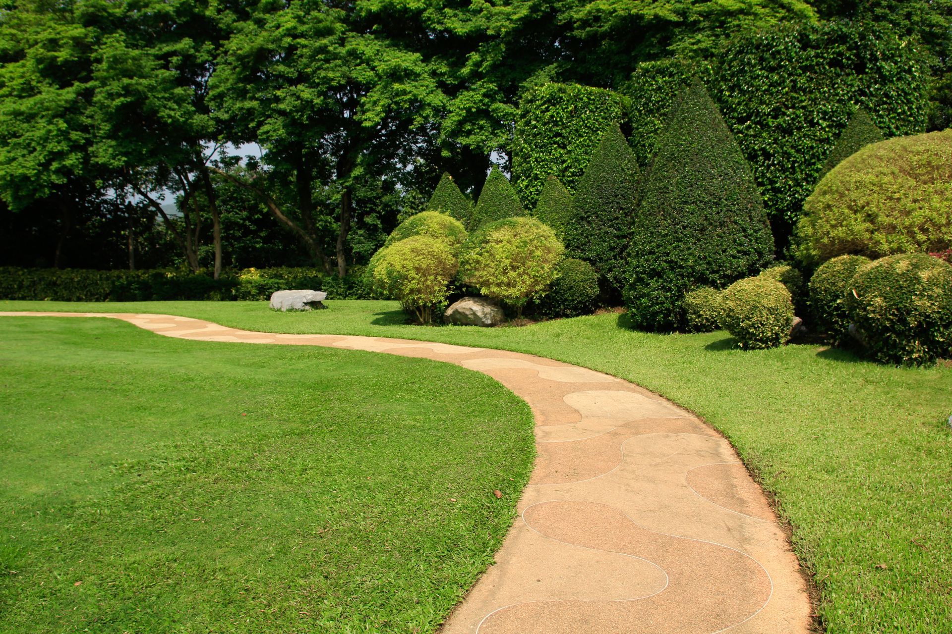 Un chemin sinueux à travers un jardin verdoyant et soigné, orné de buissons et d'arbres taillés.