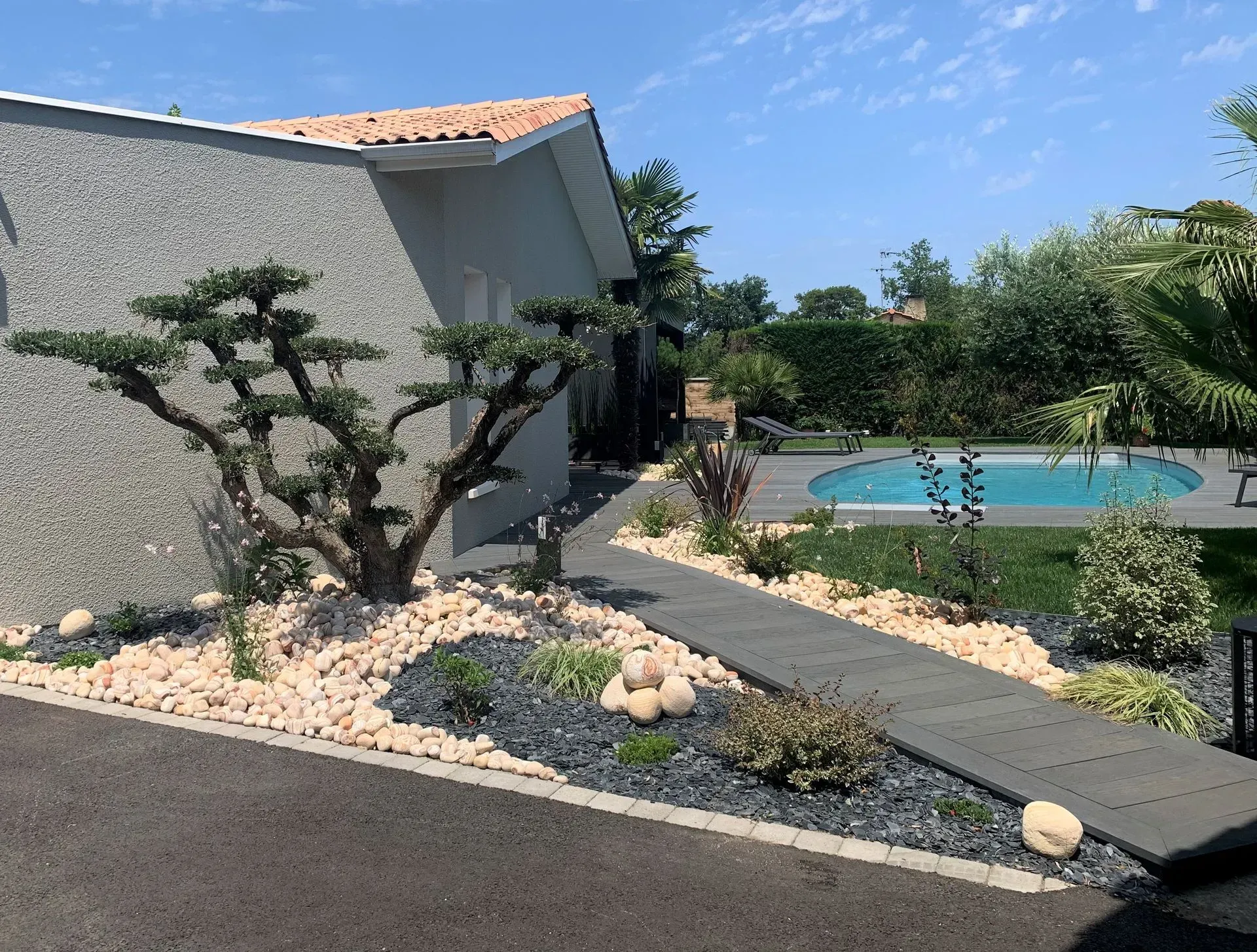Aménagement paysager avec des pierres décoratives, des plantes et un arbre taillé à côté d'une piscine.