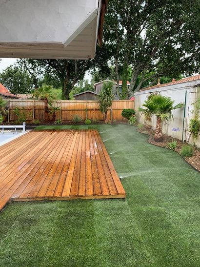Terrasse en bois avec piscine, arrosage et jardin aménagé avec des massifs de végétaux.