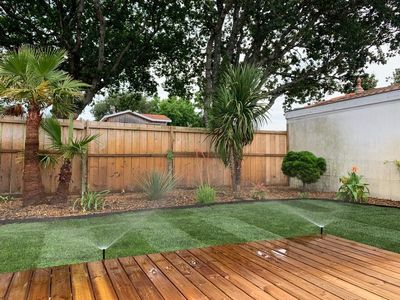 Terrasse en bois avec jardin et massif d'arbustes et arrosage automatique.