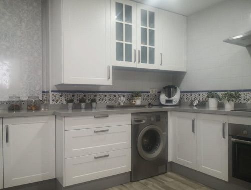 Una cocina con gabinetes blancos, una lavadora y una estufa.