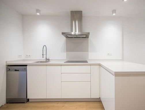 Una cocina con gabinetes blancos, un fregadero, una estufa y un lavavajillas.