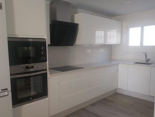 Una cocina con gabinetes blancos, un horno de estufa, un fregadero y un microondas.