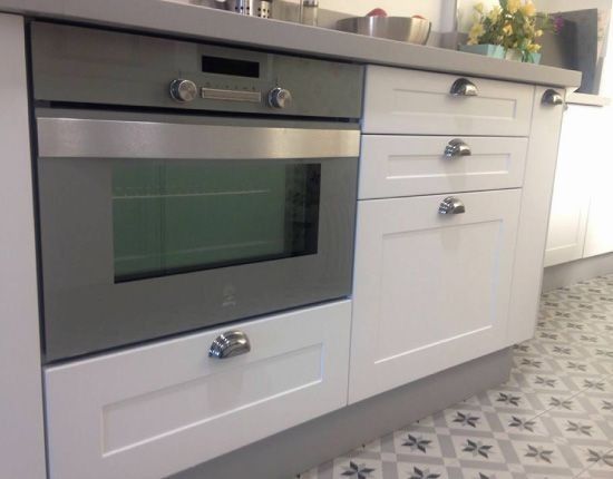 Una cocina con gabinetes blancos y un horno gris.