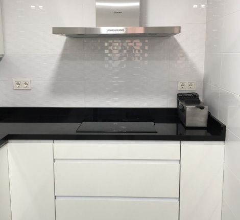 Una cocina con encimeras negras y gabinetes blancos y un horno de estufa.