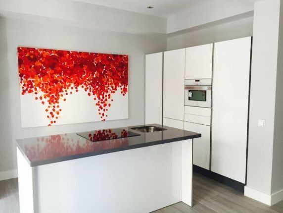 Una cocina con gabinetes blancos y una gran pintura roja en la pared.