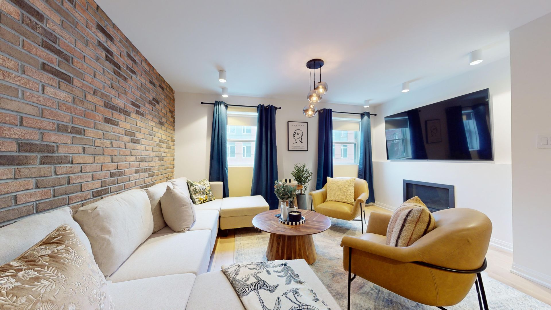 Interior view of a modern living space with a kitchen, dining area, and desk. Dark floral wallpaper, dark chairs, and wood desk.