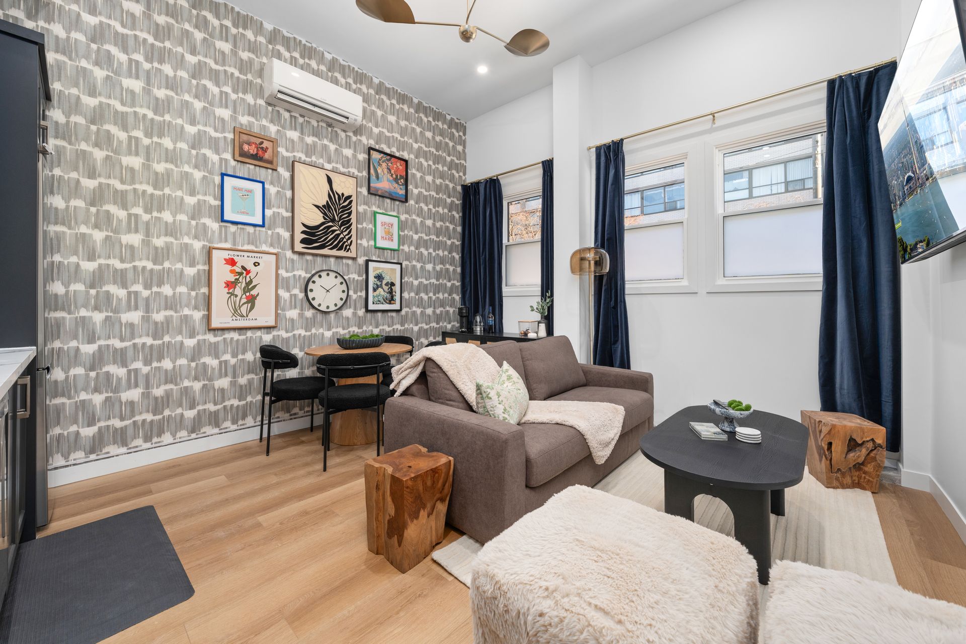 Living room with patterned wallpaper, gray sofa, dark curtains, and various art pieces.